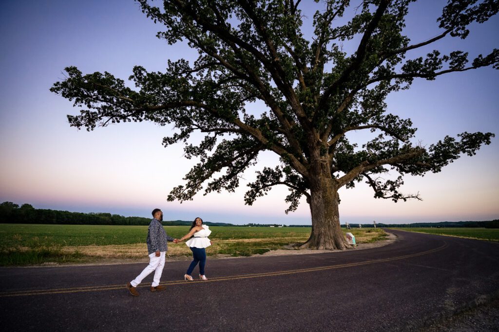 Engaged couple walks on road holding hand by the big tree near Columbia, Missouri.