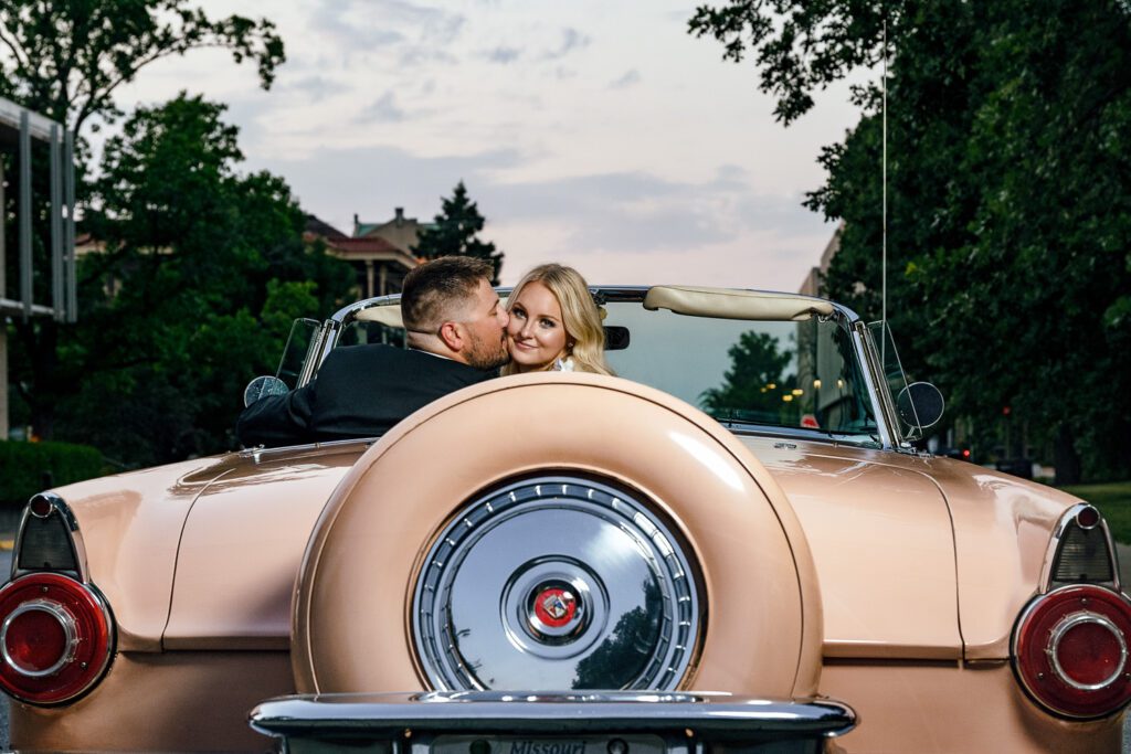 Blonde white woman looks over the back on 1955 Buckskin Thunderbird Convertible as fiancé kisses her on cheek.