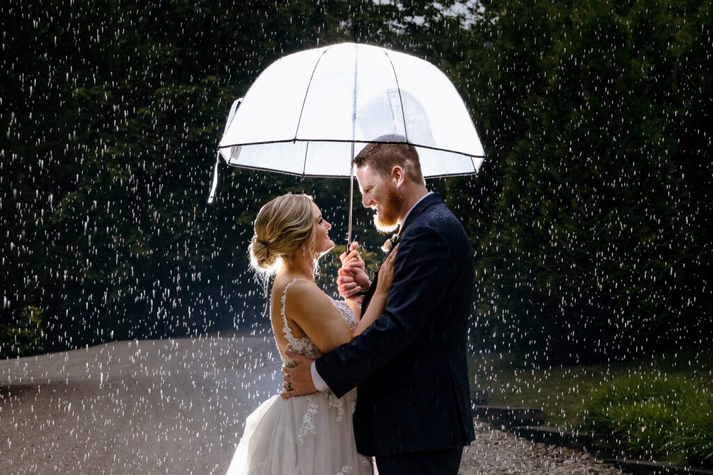 Newly weds look at each other while holding an umbrella during the rain 