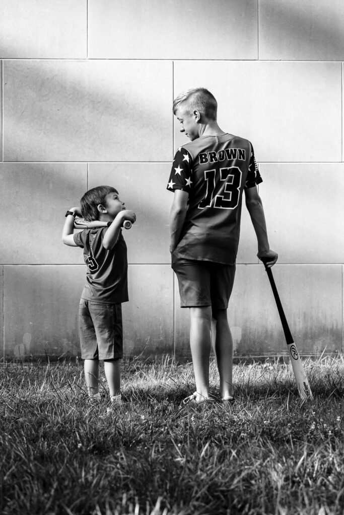 Young boy looks up to older brother while holding baseball bat.