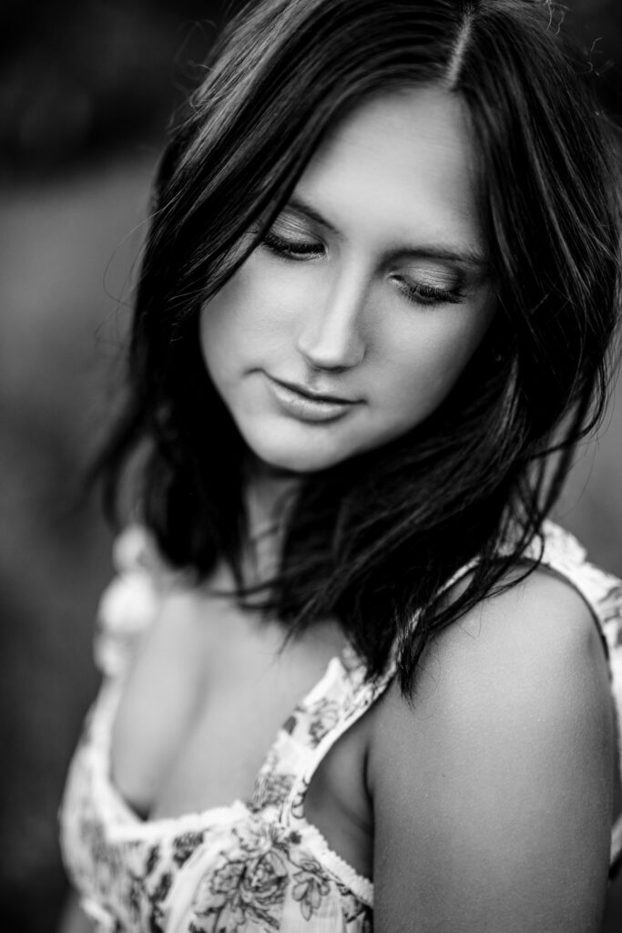 Senior Girl wearing flower top looks down shoulder.