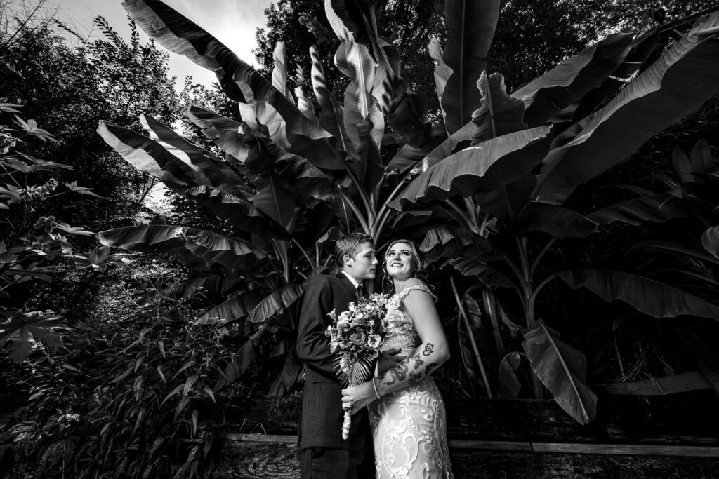 Couple pose in front of tropical plants after wedding ceremony.