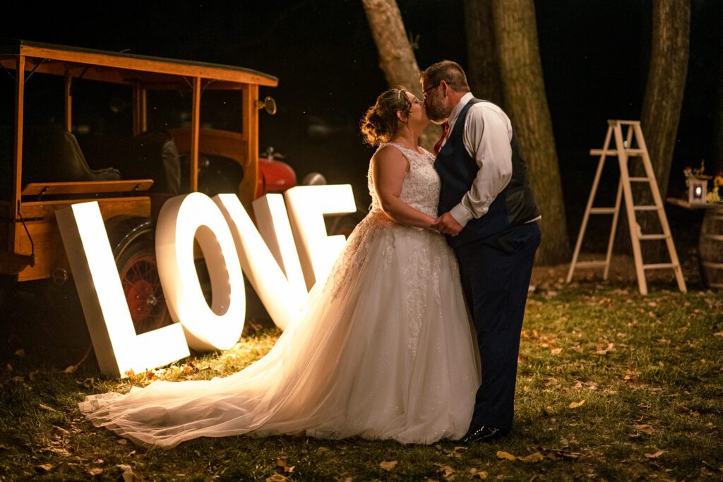 Couple kiss on their wedding day at Wildcliff Wedding in front of LOVE sign and old car.