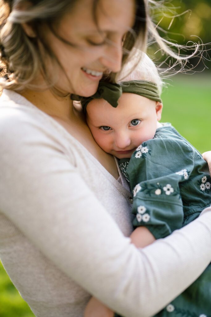 young girl looks at camera as she snuggles into her mom.