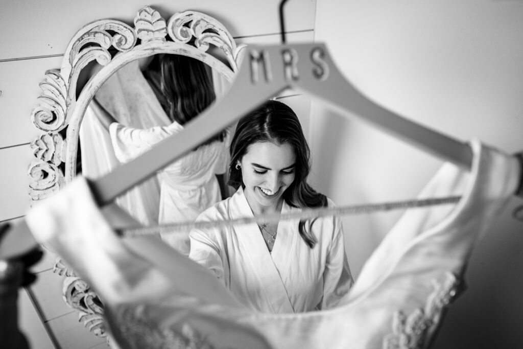 Bride looks at her dress while she is seen through a clothes hanger that says MRS.