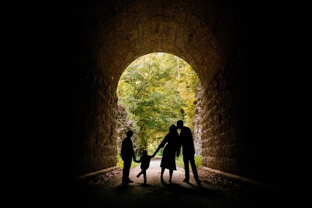 Family holds hands in Katy Trail Train Tunnel as mom and dad kiss near Rocheport, Missouri.