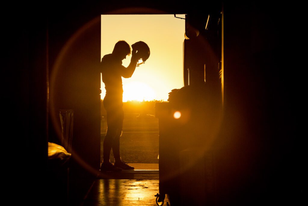 Hallsville, Missouri Football player puts on his helmet in tunnel as Sun sets producing sun flare surrounding him.