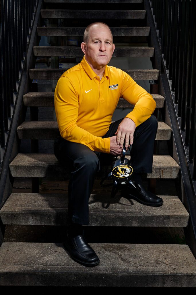 Mizzou wrestling Coach Brian Smith poses wearing yellow and black on old stair case in Columbia, Missouri.