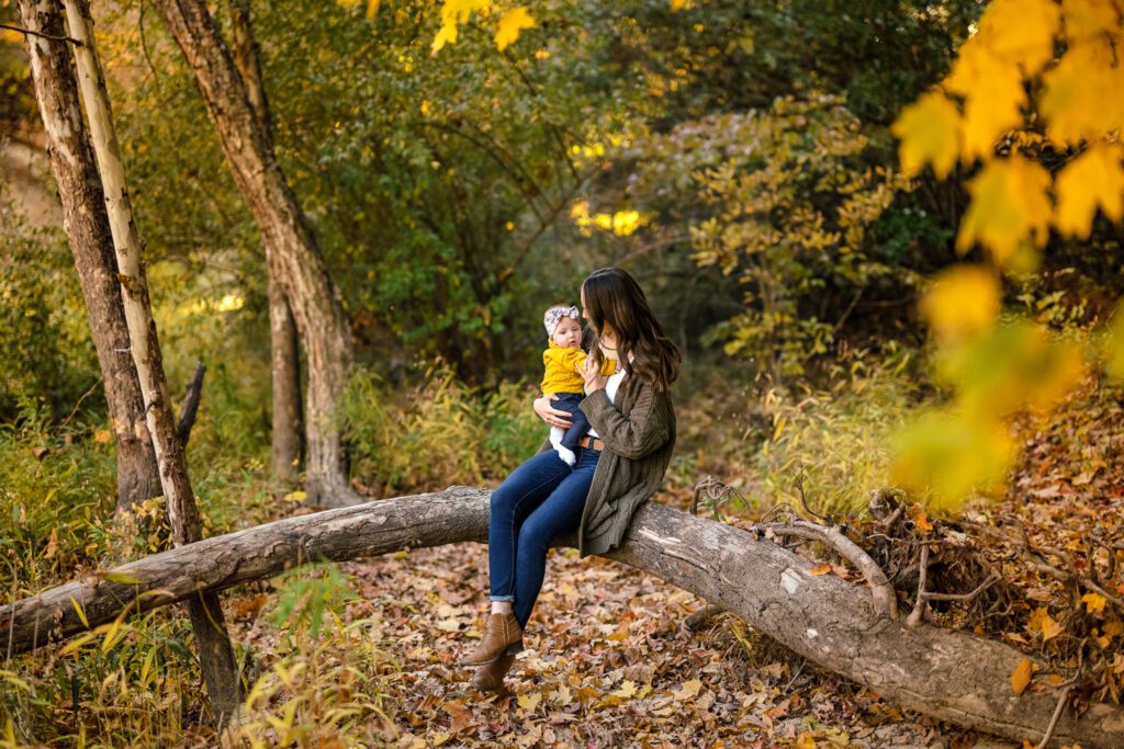 Mother kisses 6 month old daughter while sitting on log at the Pinnacles Youth Park near Columbia, Missouri.