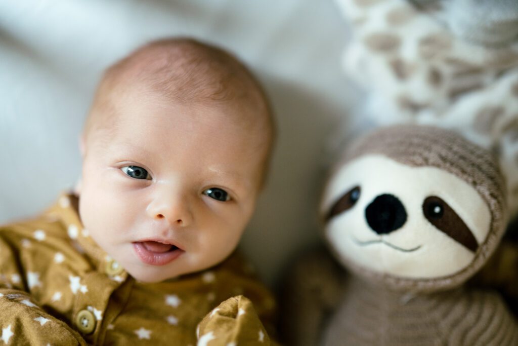Newborn with eyes open looks at camera while laying next to toy sloth.