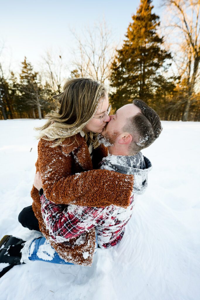 Couple kiss and frolic in the snow during a Schaefer Photography Engagement Session near Columbia, Missouri.