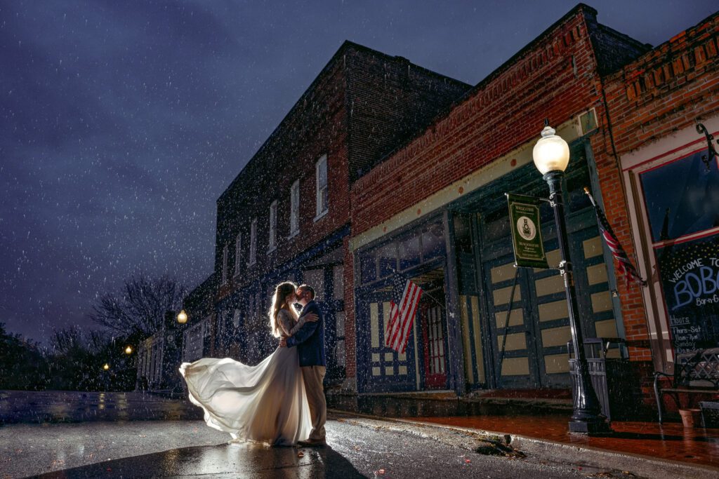 Bride and Groom kiss in the rain in small town Blackwater, Missouri while her wedding dress flips in the wind at Wildcliff Weddings.