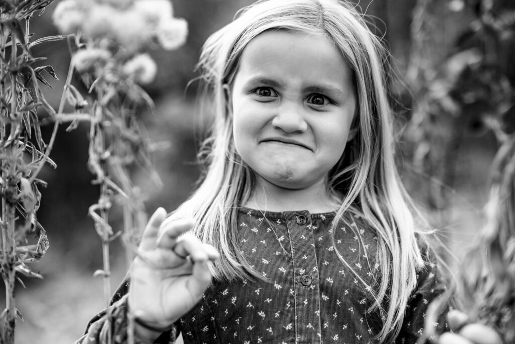 Little girl makes hilarious funny face while looking at nature flowers