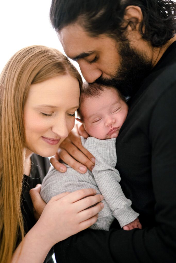 New parents snuggle baby boy tightly while hugging
