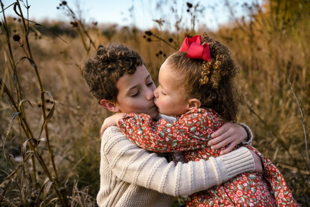 Two small children kiss in field during family photo session in Columbia, Missouri.