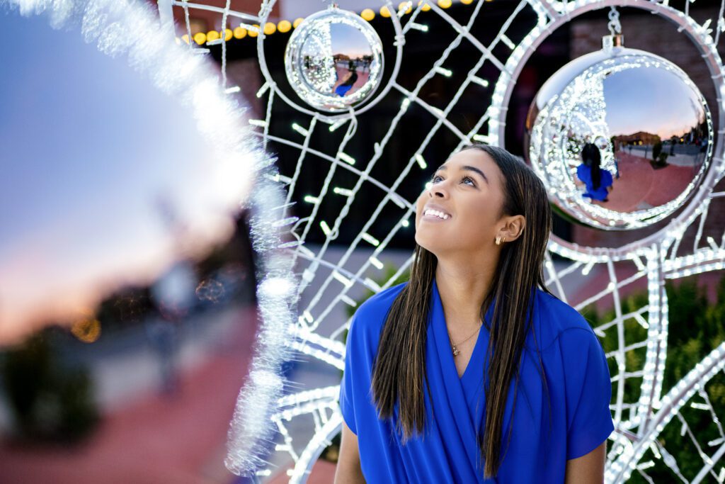 Senior girl wearing blue dress looks in awe at silver Christmas decorations in Columbia, Missouri.