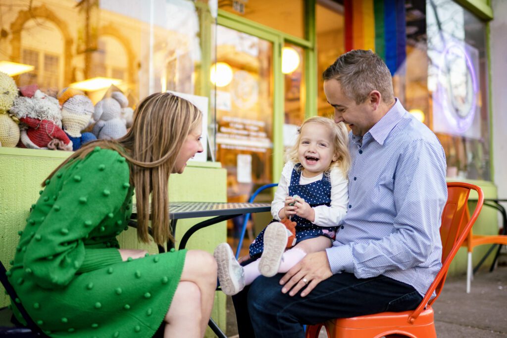 Family with young daughter laugh in front of green store front in downtown Columbia, Missouri.