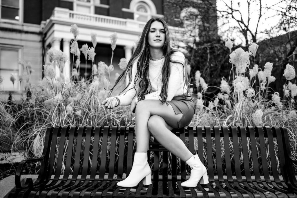 Senior girl with white boots sitting on black metal bench at University of Missouri Columbia.