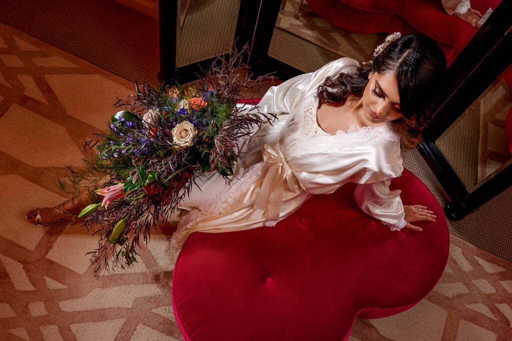 bride lounging on pink velvet stool in large flower bouquet in silk robe