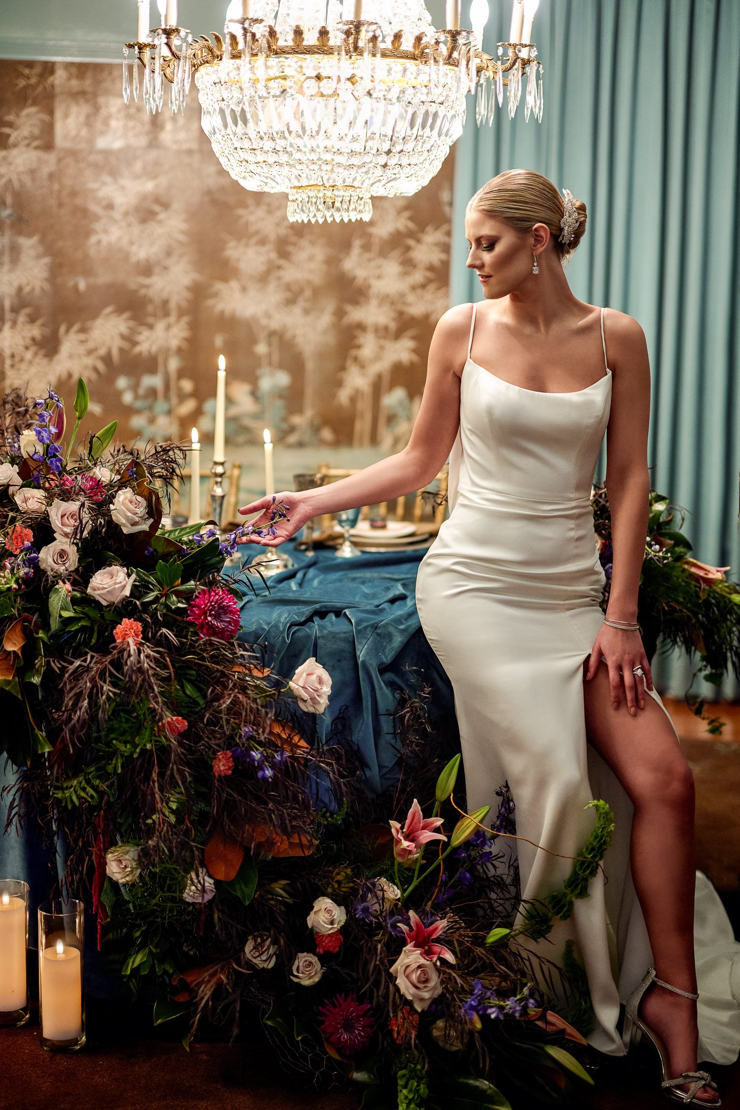 bride touching flowers in silk gown on dark and moody sweetheart table