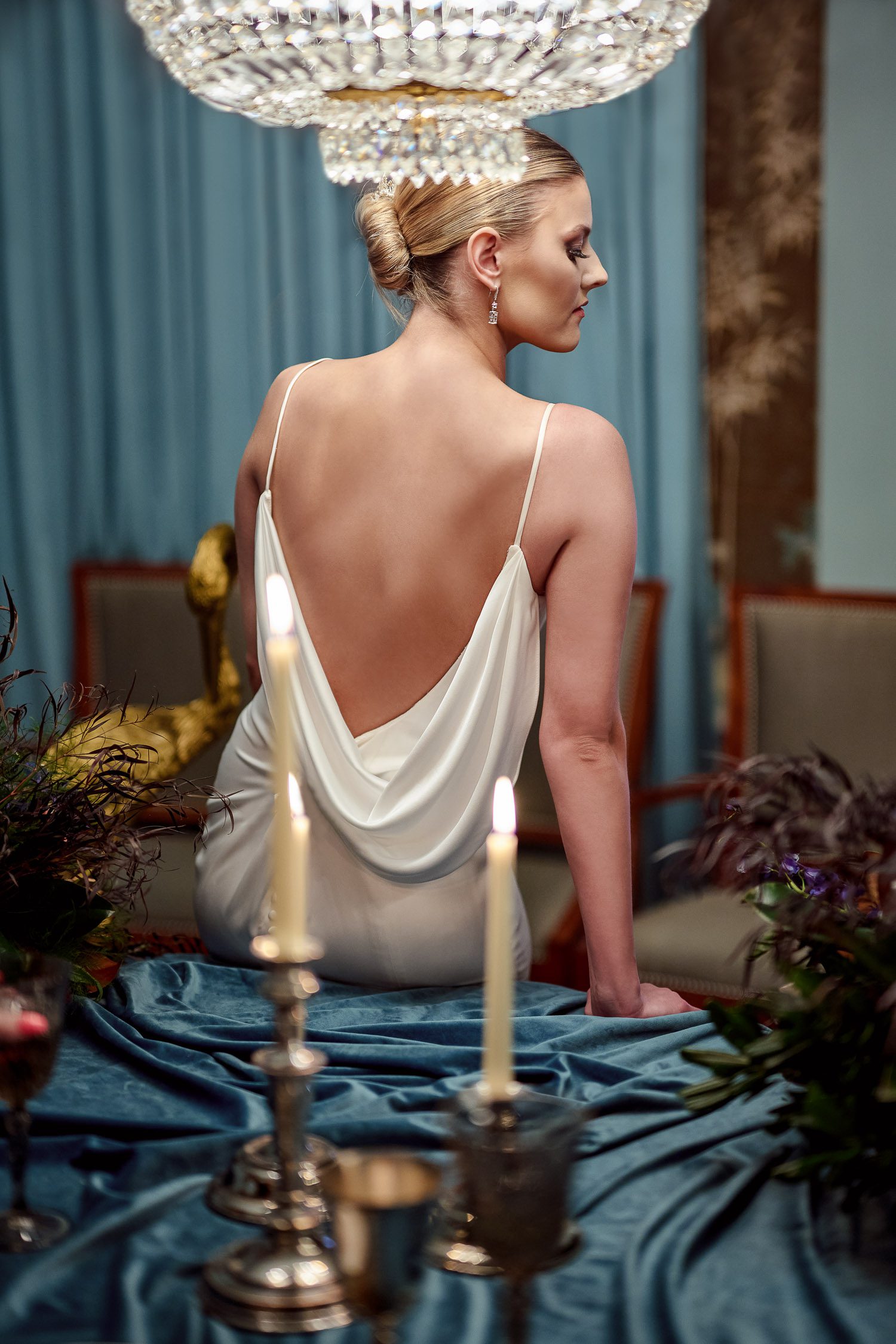 back of bride in silk cowl back dress and slicked back bun with blue velvet table and candles