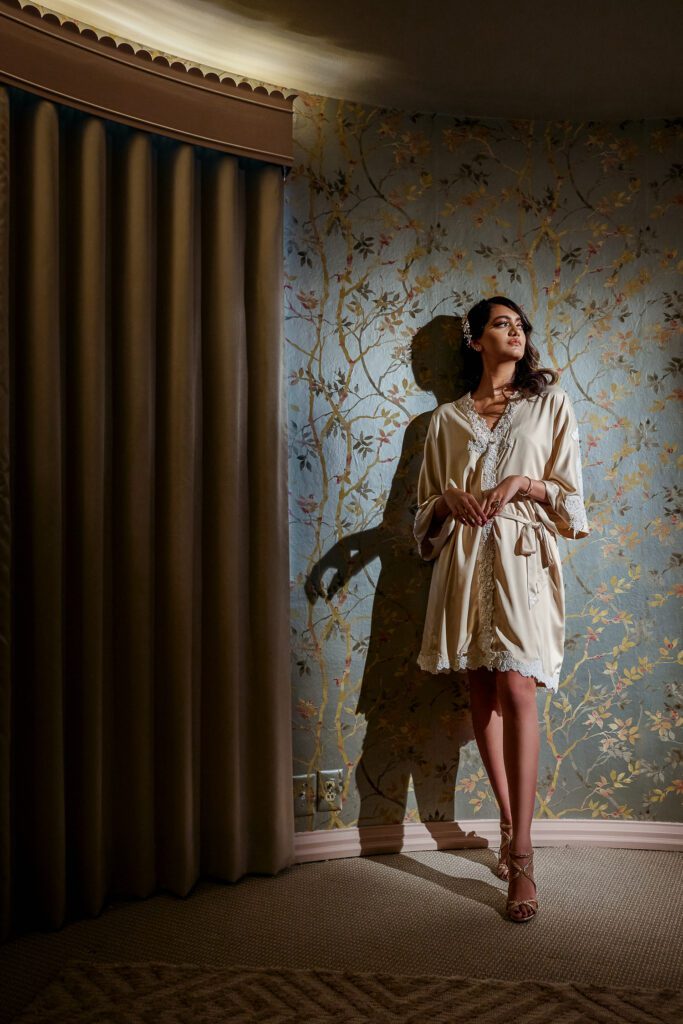 bride in silk robe leaning against wallpaper room in Jimmy Choos