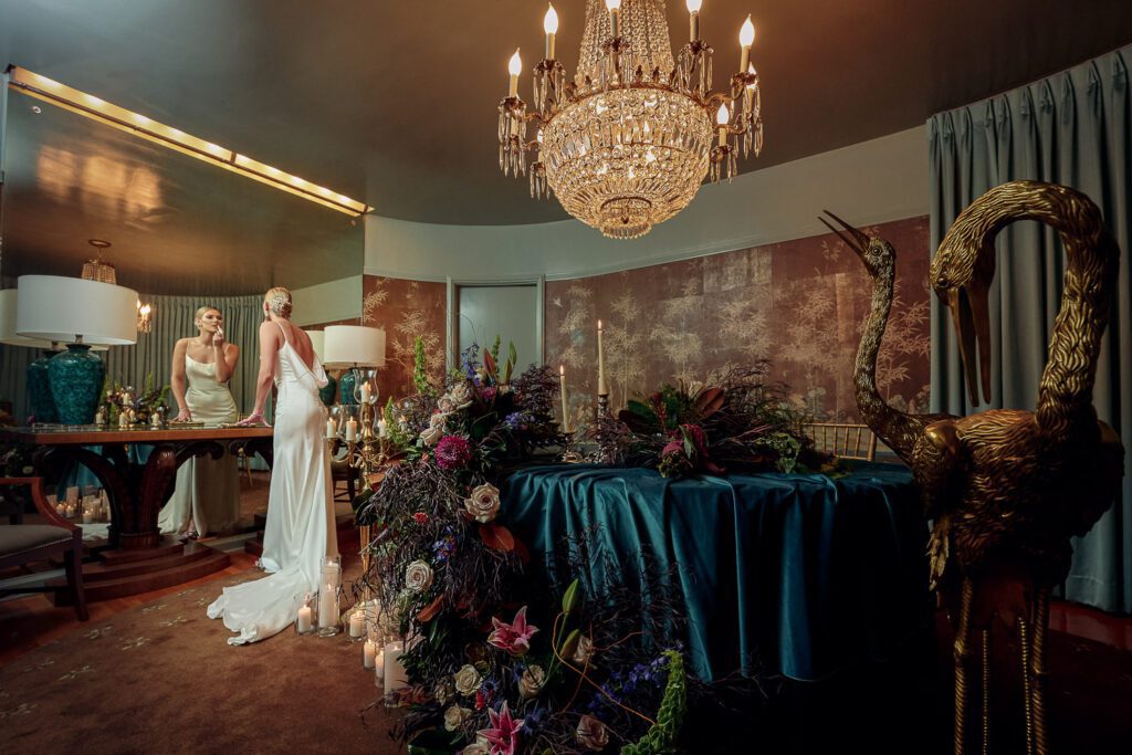 Bride touches up lipstick in mirror and art deco dark and moody table set.