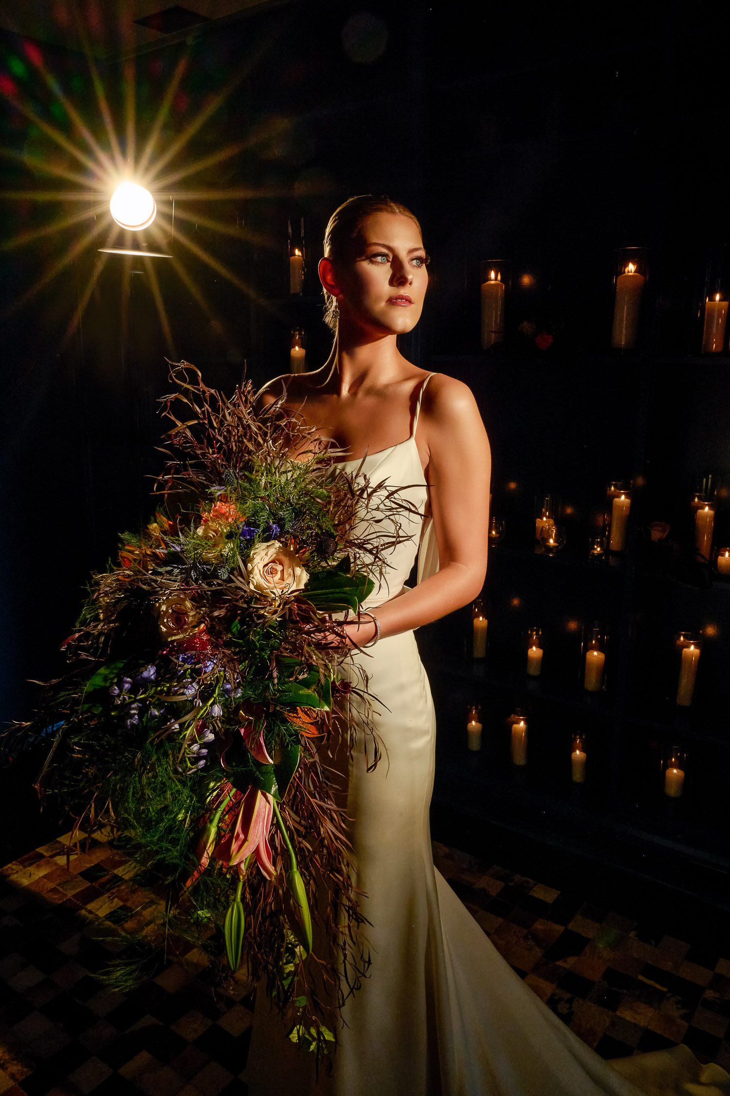 bride in silk gown with dark and moody bouquet in front of candle wall and old hollywood lighting