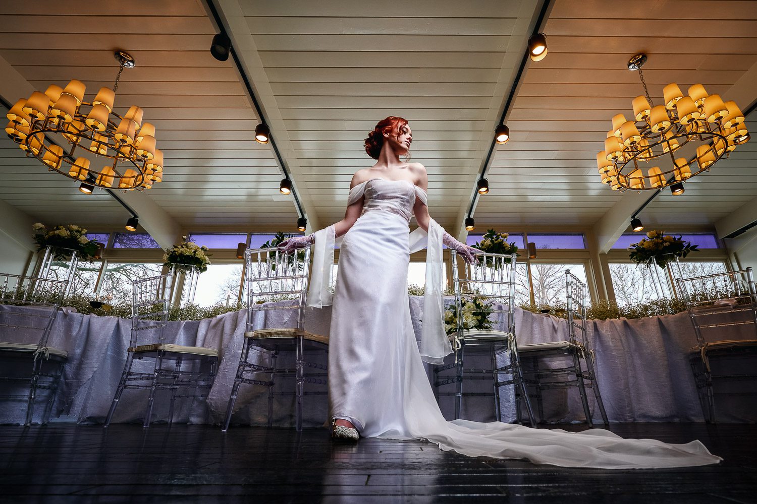 Bride stands in Chatol Ballroom with yellow chandeliers and acrylic chairs in Centralia Missouri.