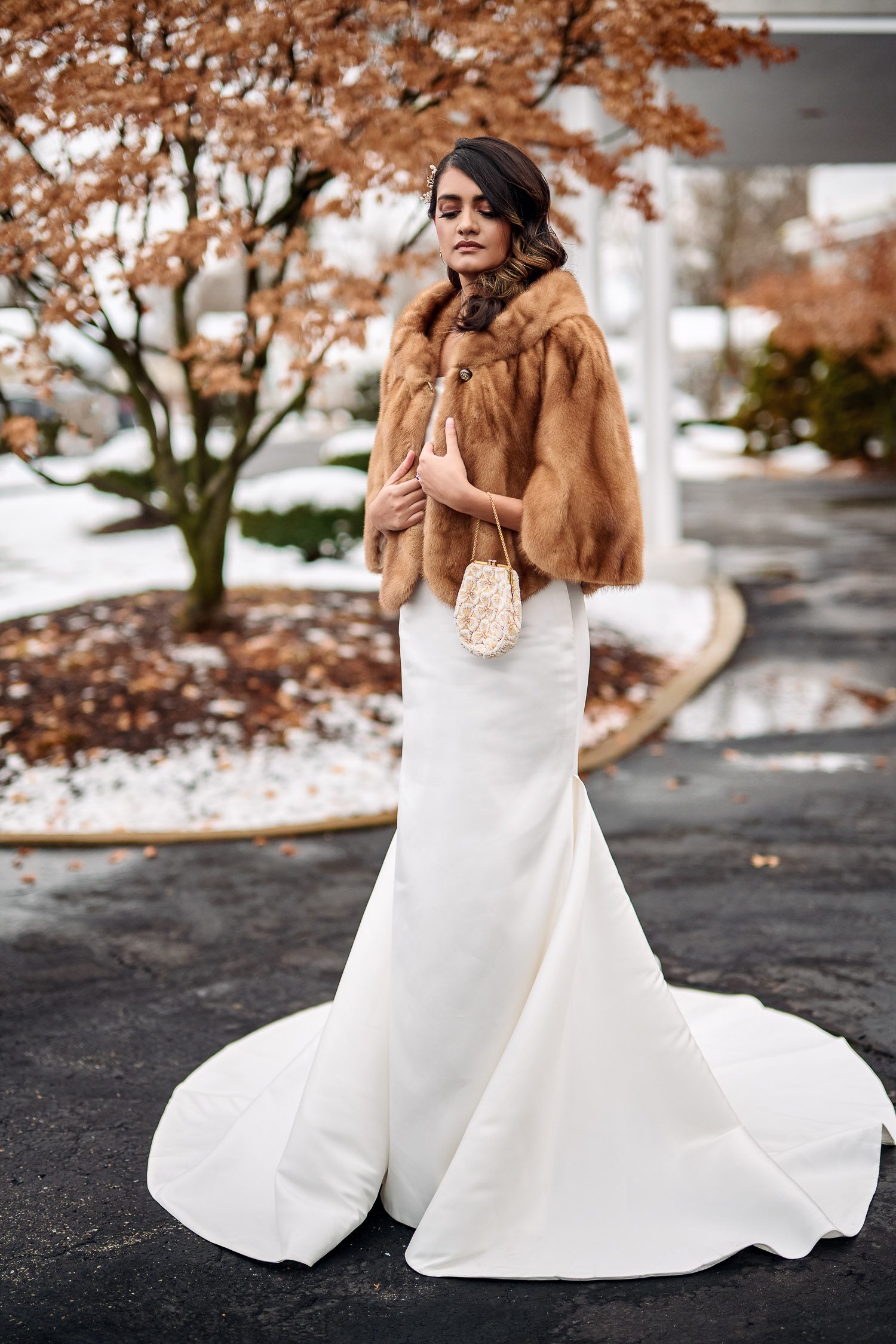 bride in fur cape with snowy background and vintage hand bag