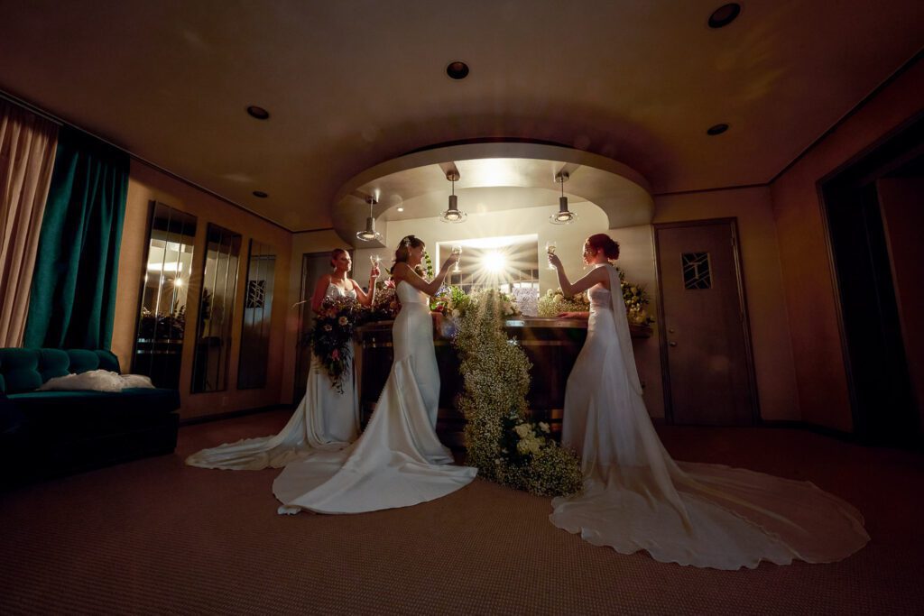 three brides toasting each other in gowns on floral vintage bar