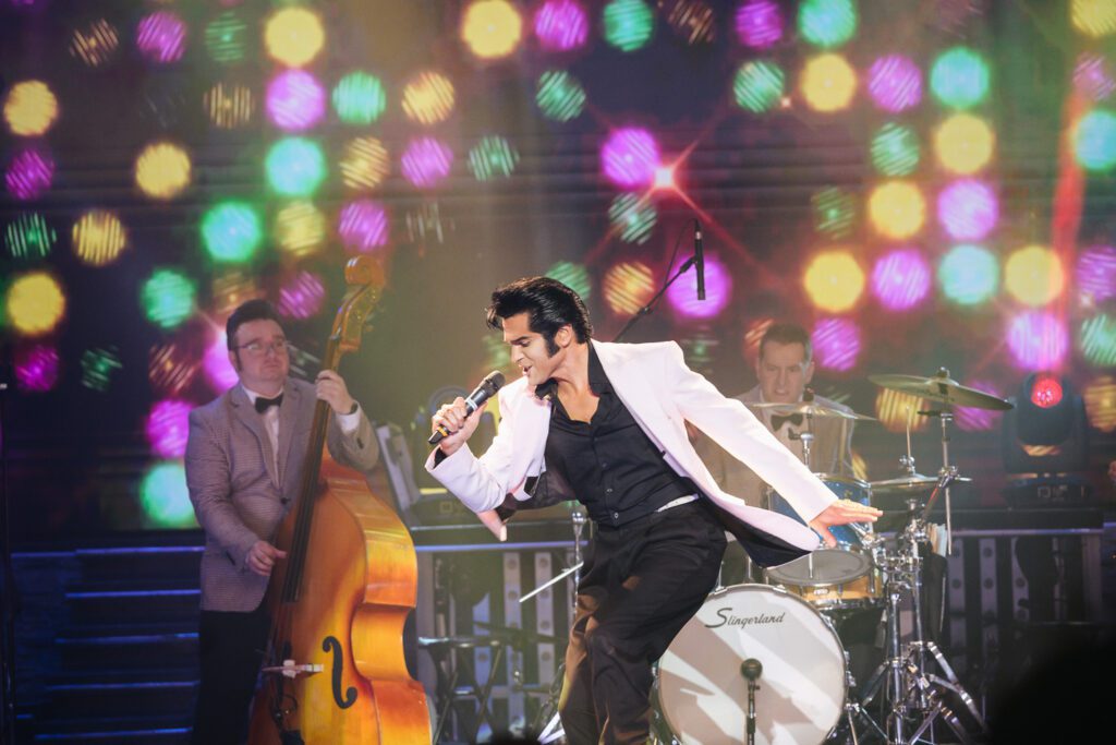 Dean Z performing as Elvis Presley in pink blazer on stage lit up with colorful lights in Branson, Missouri.