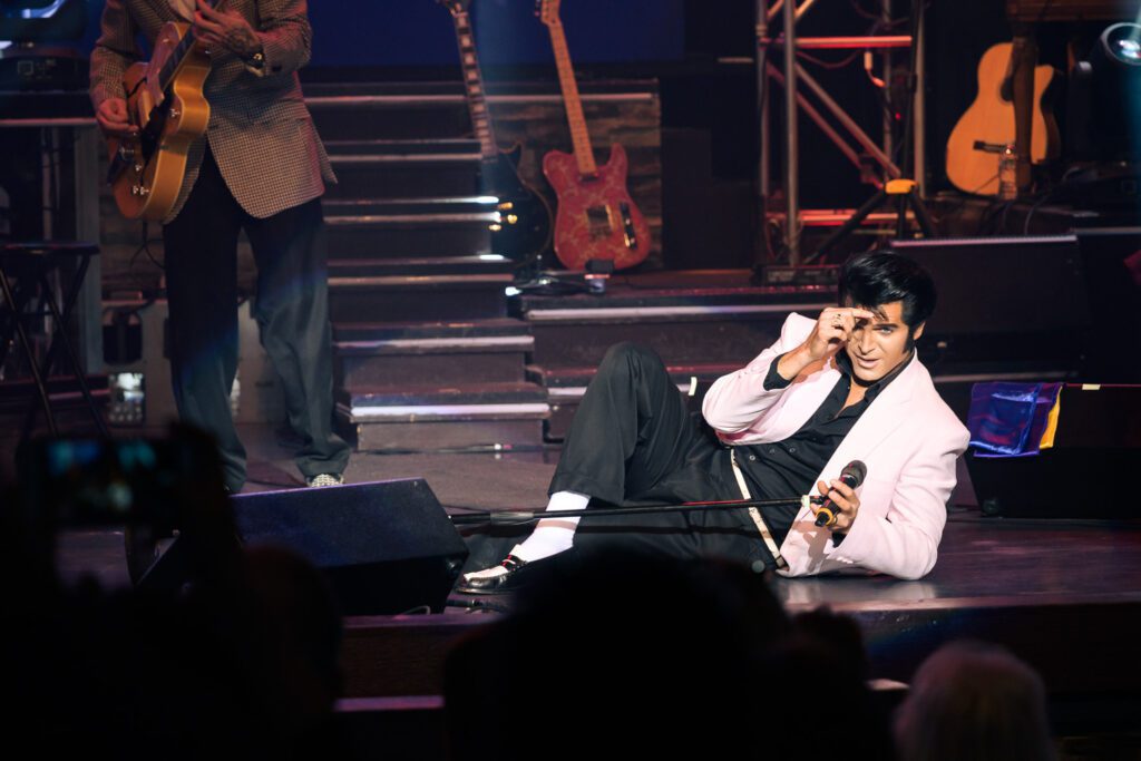 Dean Z performing as Elvis Presley in pink blazer laying on stage in Branson, Missouri.