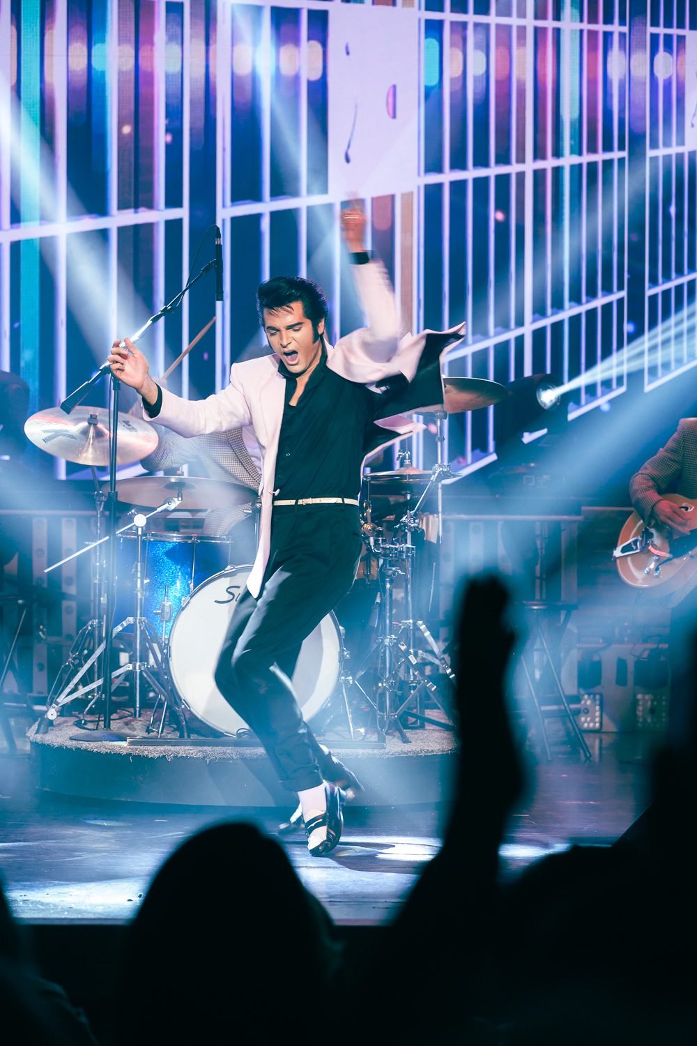 Dean Z dancing to 1950s Elvis music while performing as Elvis Presley in pink blazer on stage lit up with colorful lights in Branson, Missouri.