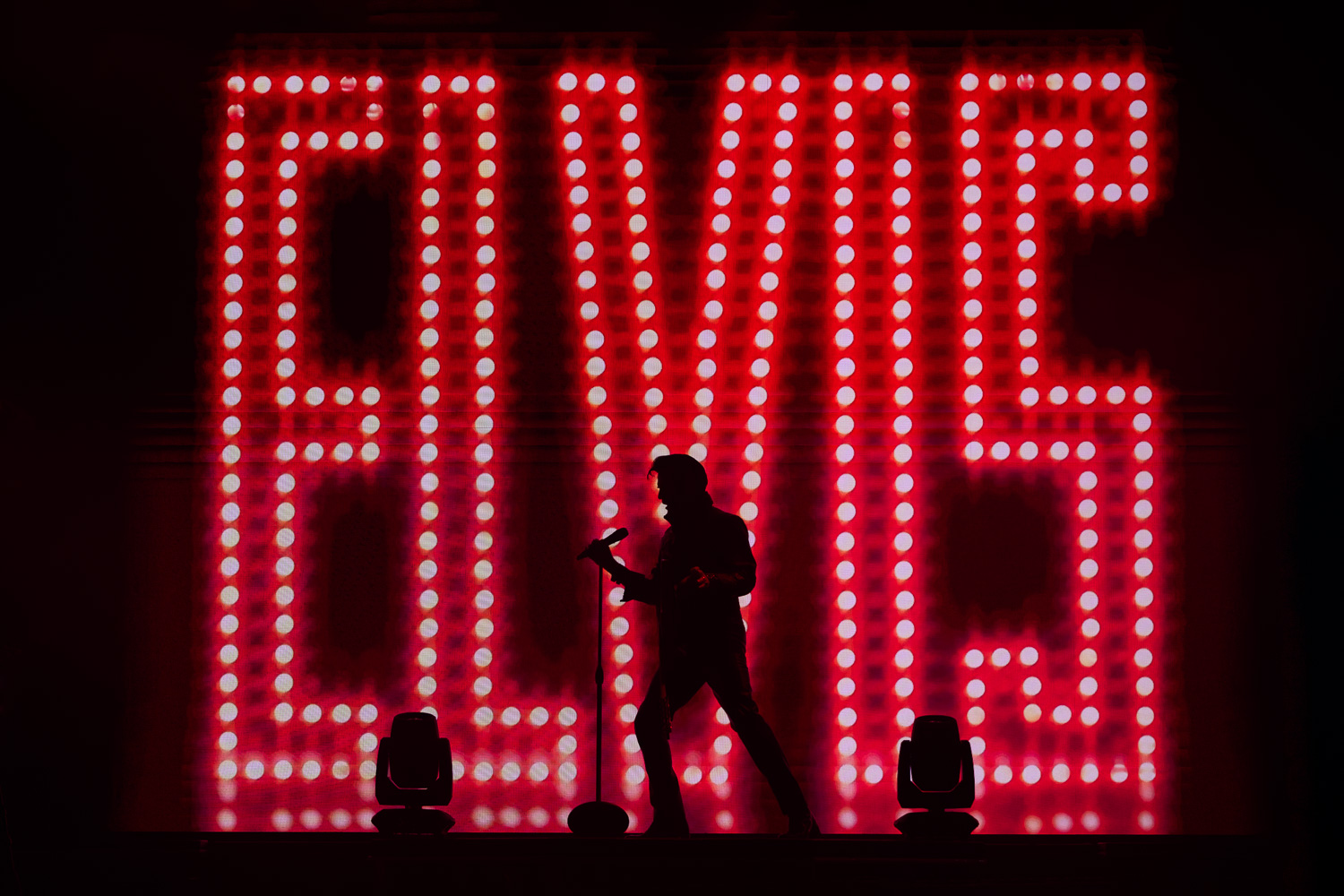 Silhouette of Dean Z performing as Elvis Presley in front of big red light letters spelling Elvis.