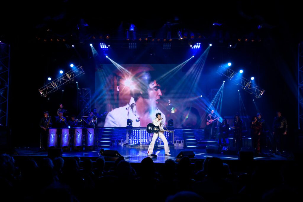Dean Z performing as Elvis Presley while the real Elvis is on screen behind him.