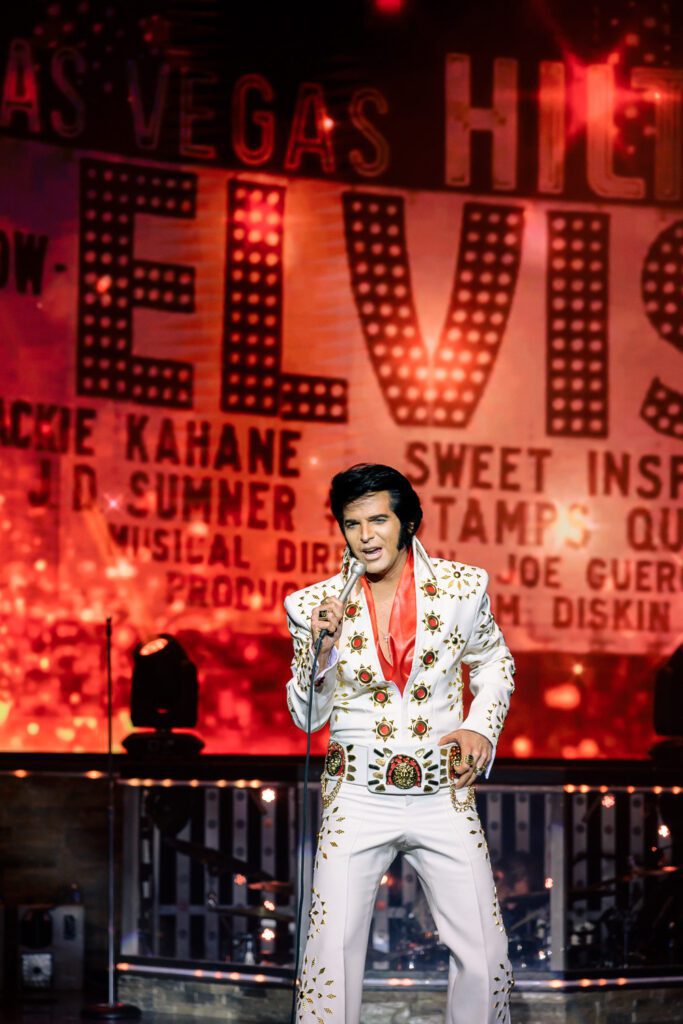 Dean Z wearing a white jump suit as he performs as Elvis Presley during the 1970s Hilton Las Vegas residency.