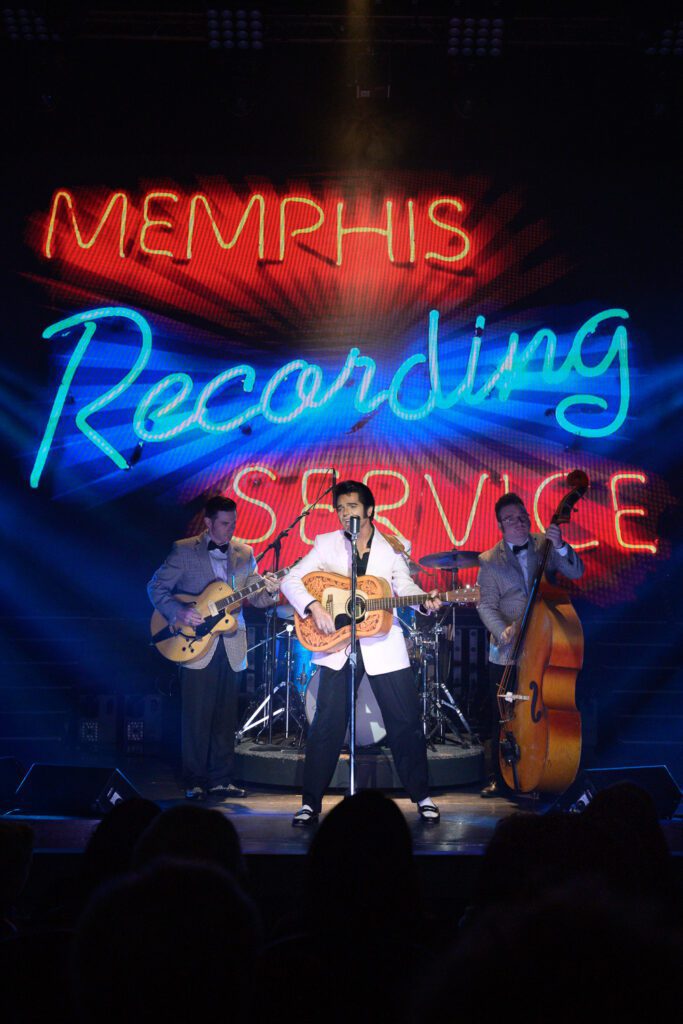 Memphis Recording Service neon light sign behind Dean Z as Elvis Presley playing guitar with two other musicians in Branson, Missouri by Schaefer Photography.