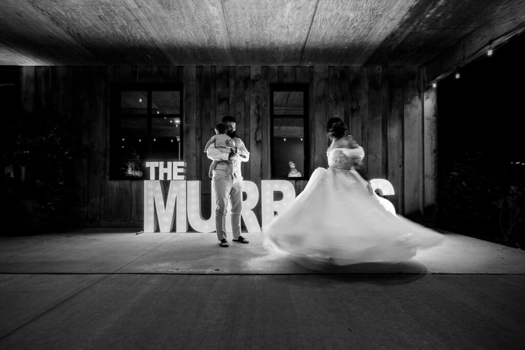 bride dances in front of last name sign with husband and daughter watching