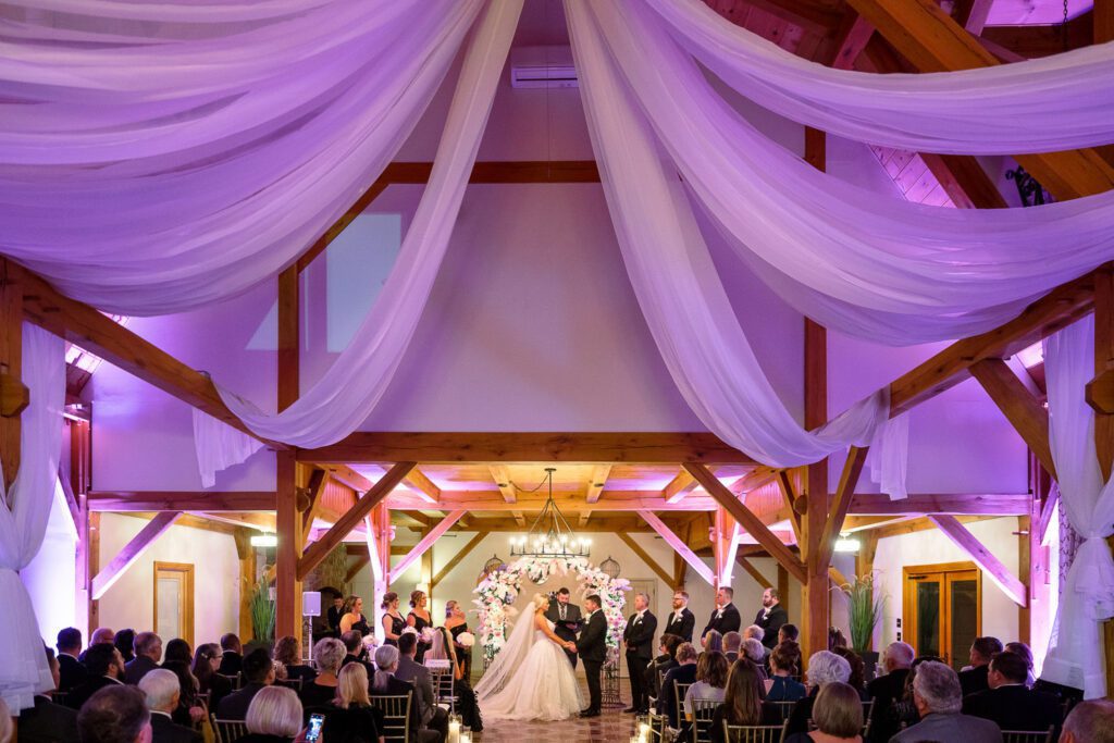 Beautiful wedding ceremony with white fabric draping from ceiling with pink lights and roses
