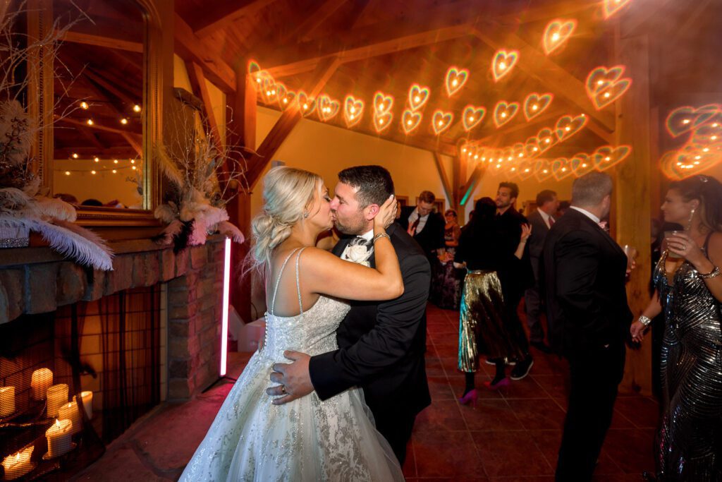 bride and groom kiss on dance floor with lights transformed into hearts with a filter over camera lens.