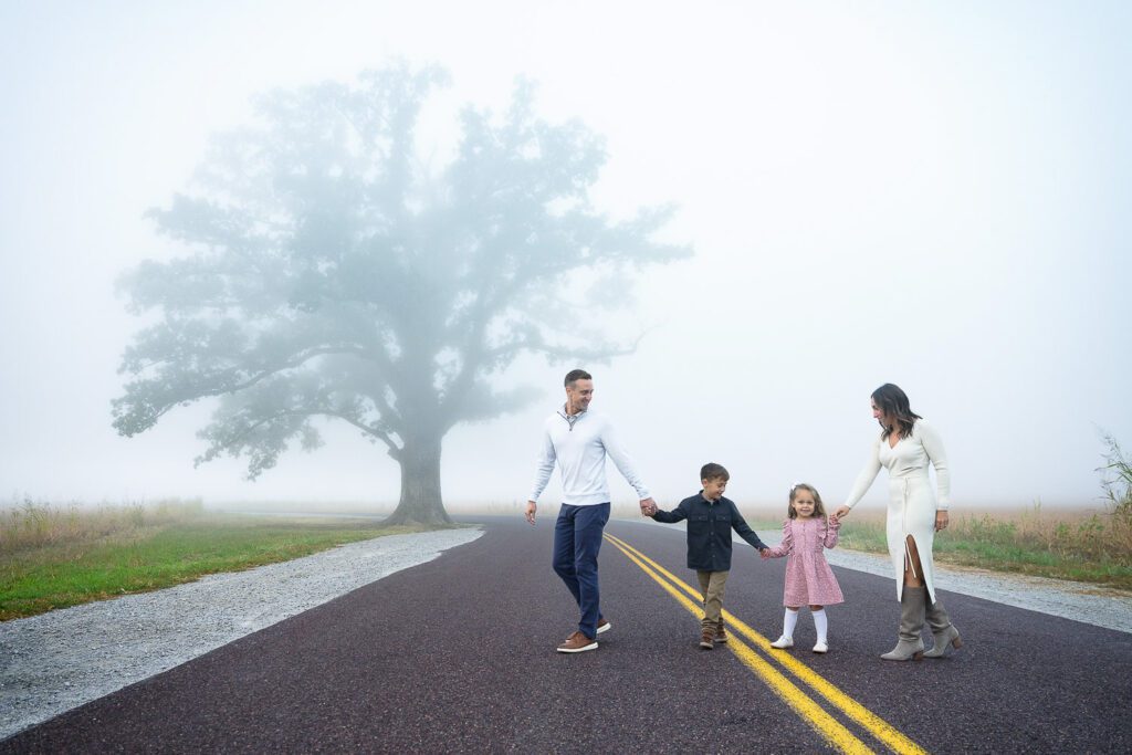 Family holding hands walking in front of fog covered big tree at mcbaine