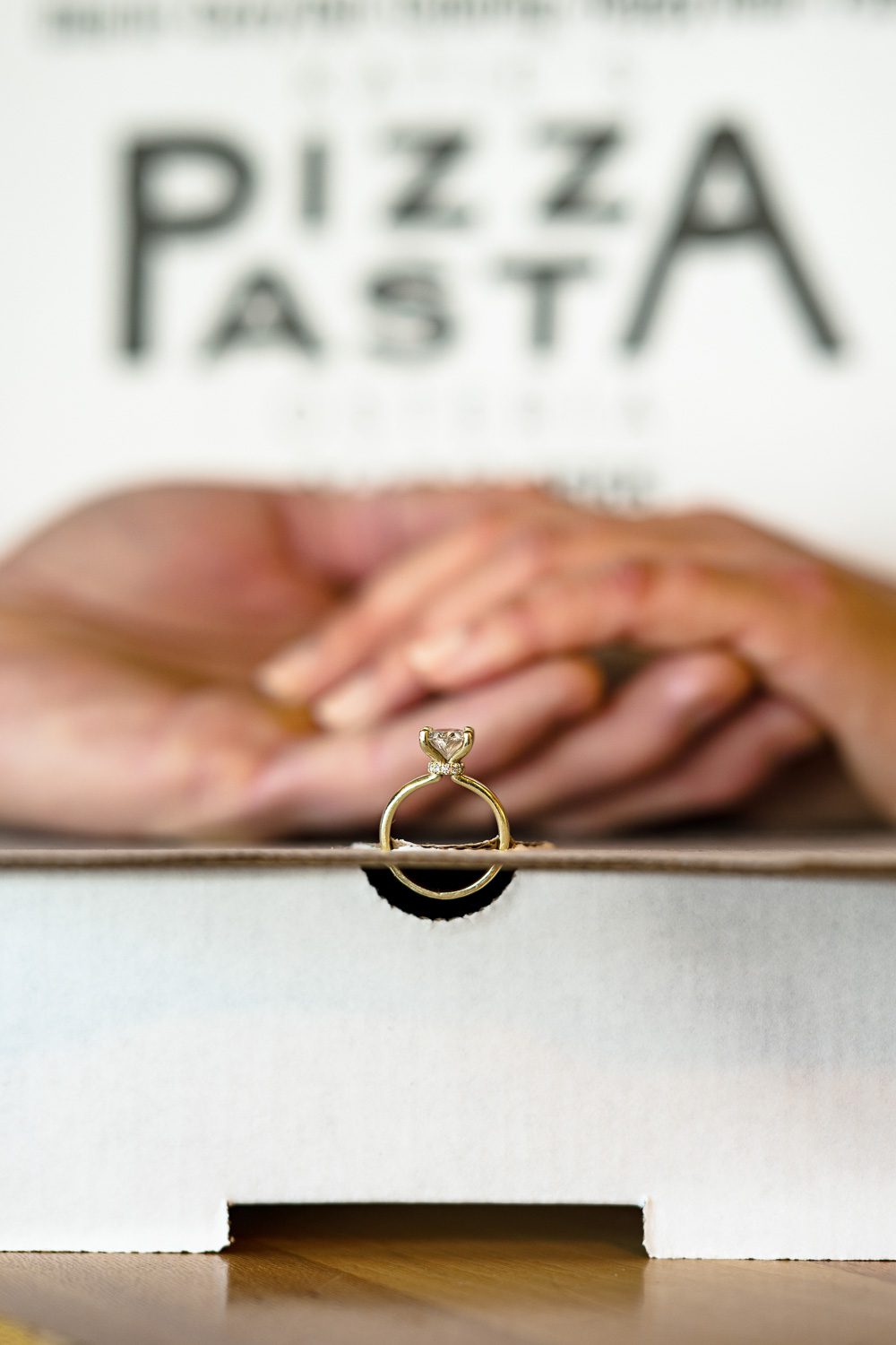 engagment ring in pizza box with couple holding hands in background