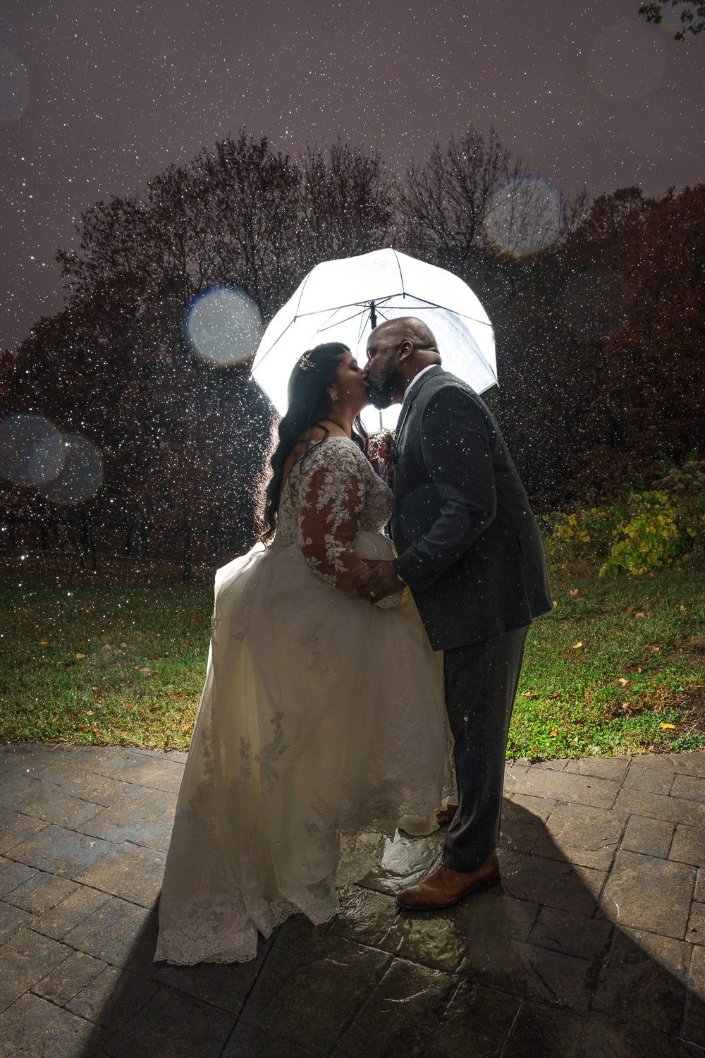 black couple kiss on their wedding day under an umbrella with rain drops