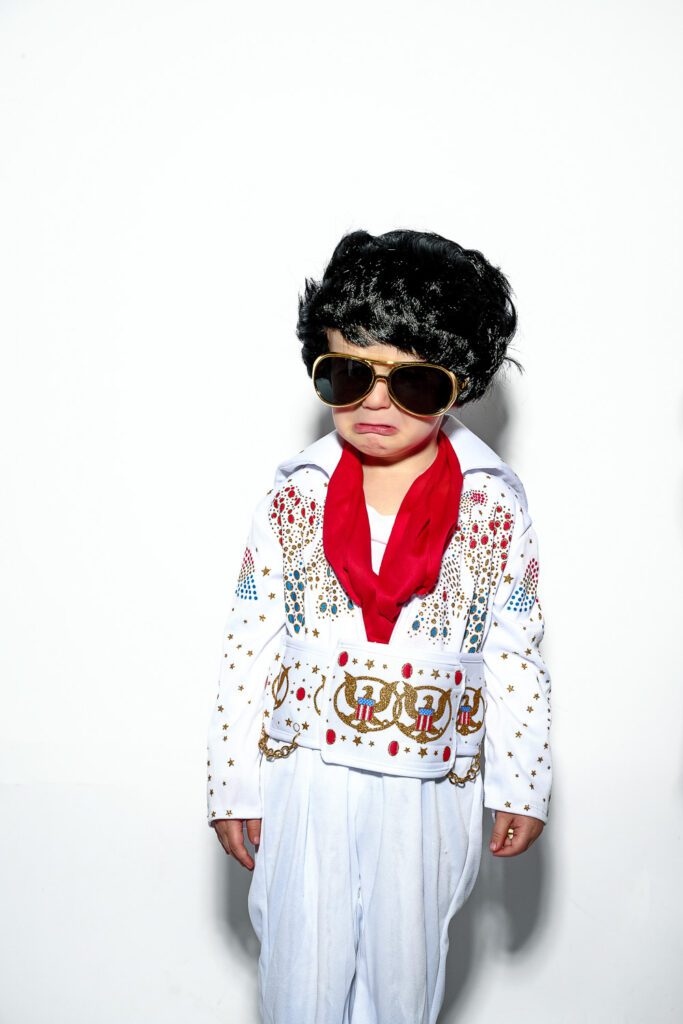 a young boy dressed as elvis looks sad on white background