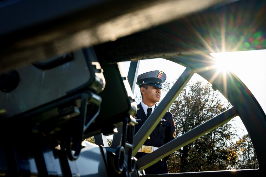 A Missouri Military Academy Senior in uniform stands behind a canon