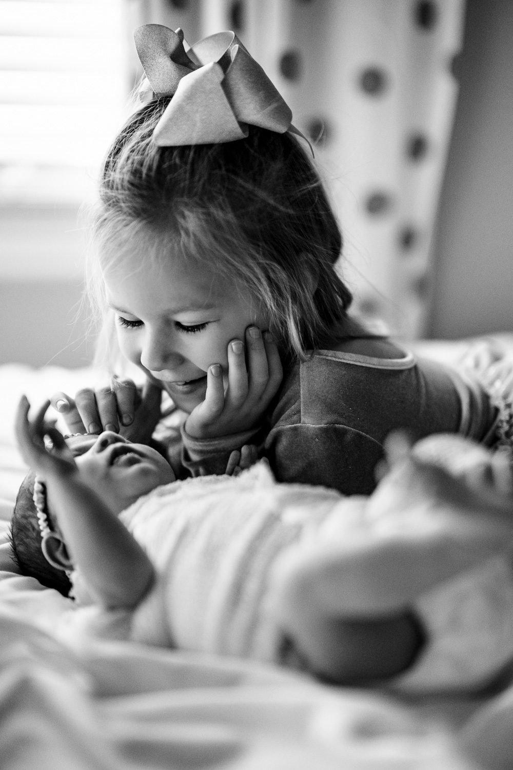 big sister smiles at newborn baby laying down on bed