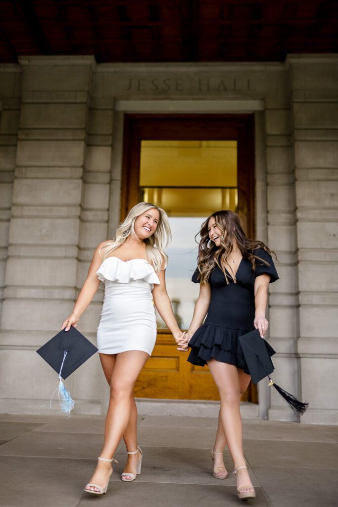 two sisters hold hands carryng mortar board graduation caps at mizzou