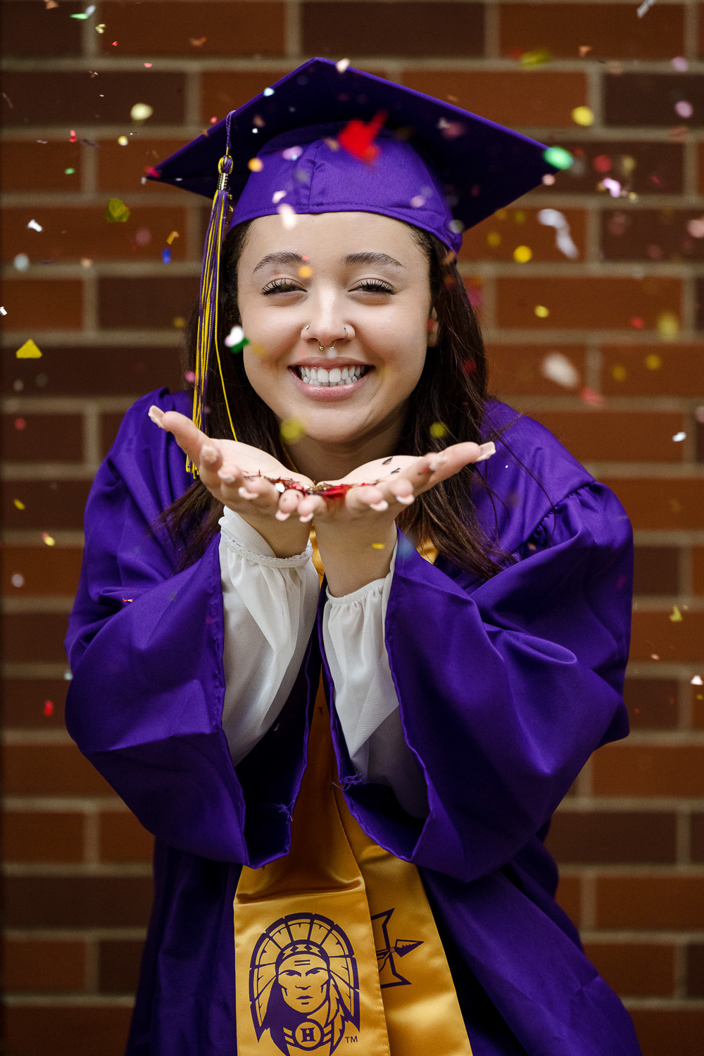 Hallsville high school senior girl blows confetti at camera wearing purple graduation gown and cap