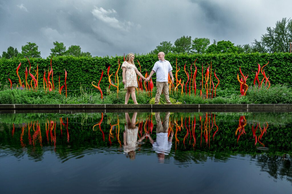 Engaged couple hold hands in front of reflecting pool with chihuly glass at st louis botanical gardens